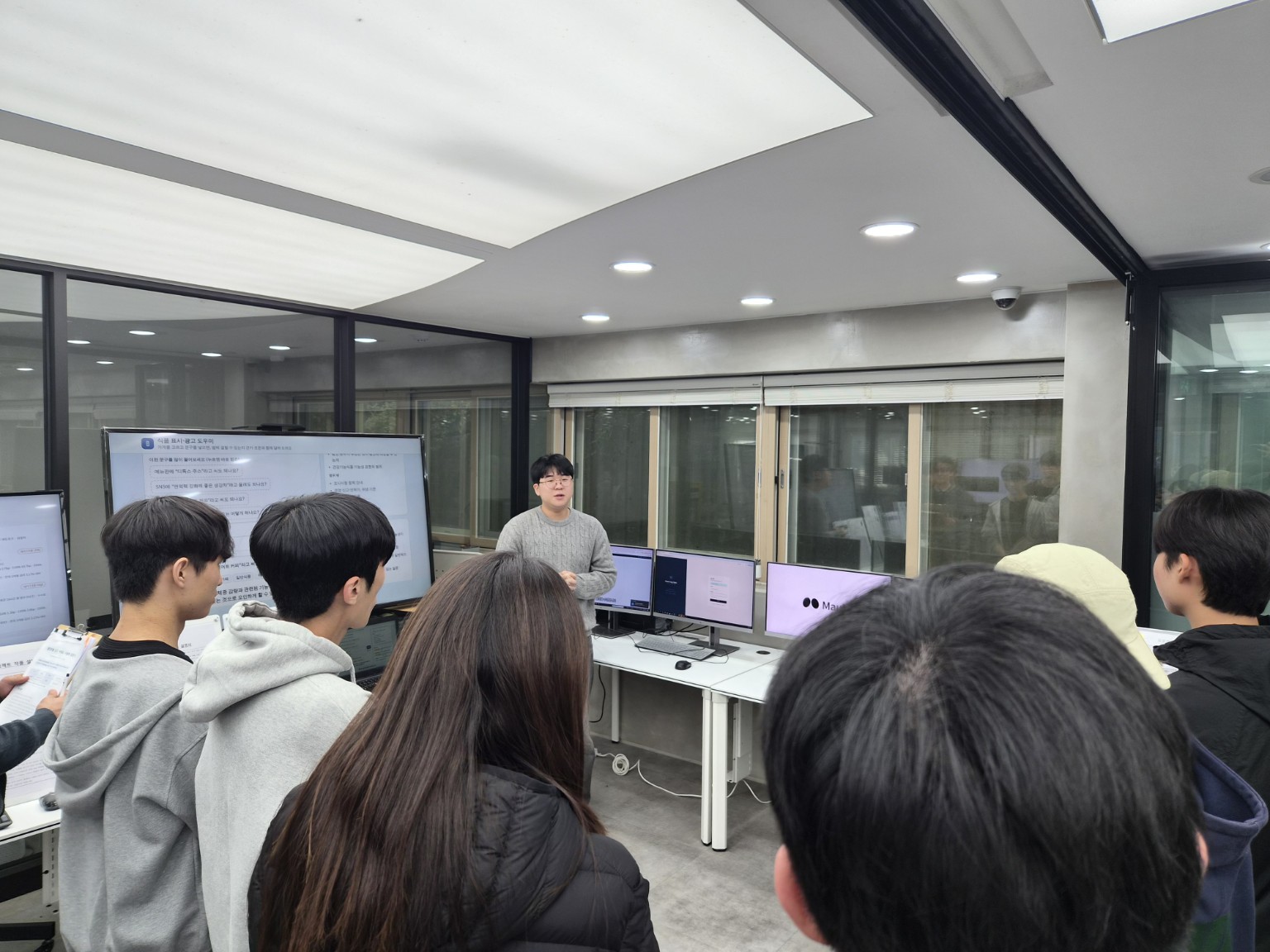 강의실에서 한 학생이 프로젝트 화면을 띄우고 다른 학생들에게 개발 결과를 설명하는 모습